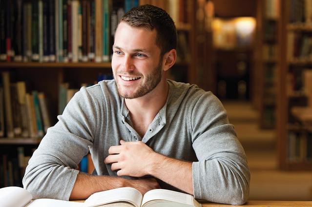 A man at the library smiling with books on the table.
